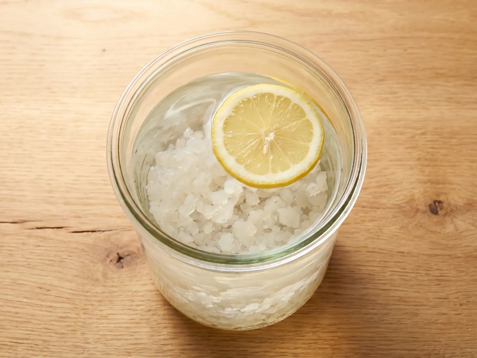 Vista dall&rsquo;alto di un barattolo con acqua, grani di kefir e una fettina di limone in superficie.