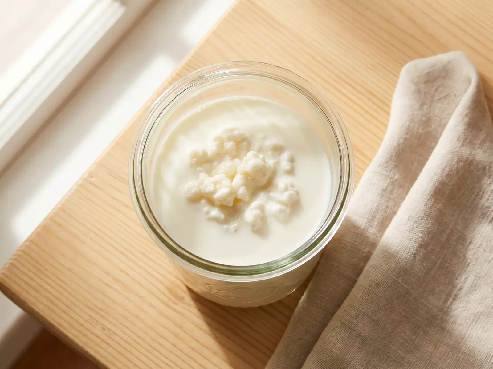 Vista dall&rsquo;alto di un barattolo di kefir di latte in fermentazione su legno con un panno di lino.