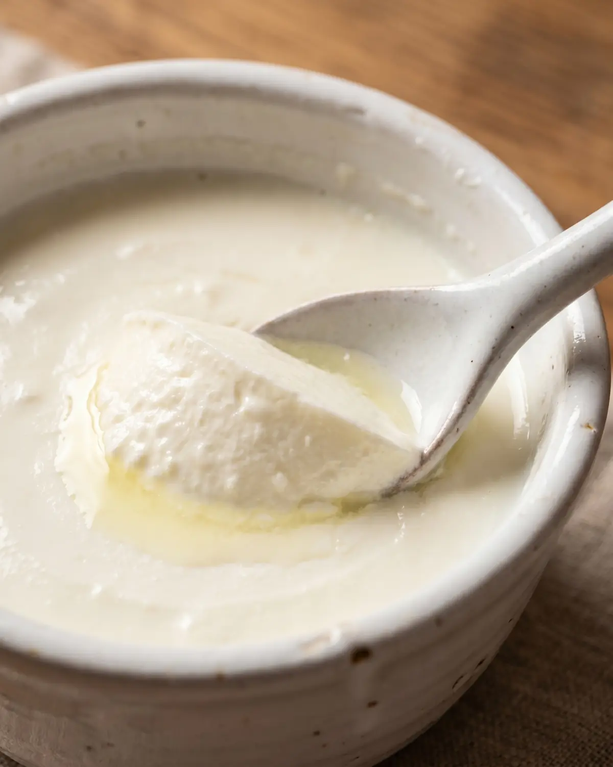 Primo piano di yogurt compatto separato con il cucchiaio, con taglio netto e poco siero lucido.